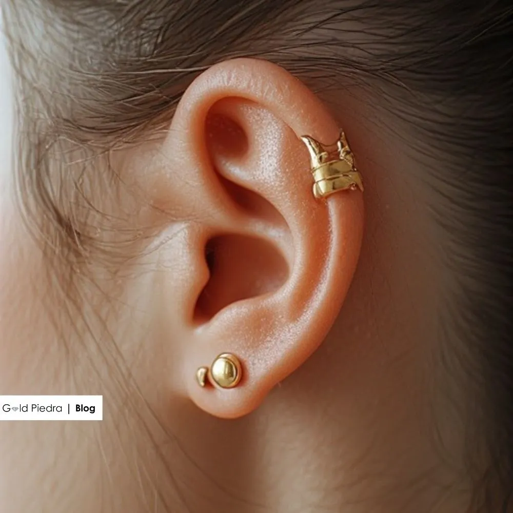 Altın top küpe ve kıkırdak bölgesinde konumlandırılmış altın piercing.