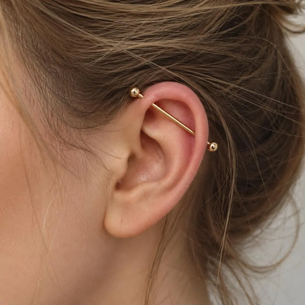 Kulağın üst kısmında helix ve forward helix bölgelerini bağlayan 14 ayar altın industrial piercing uzun barbell tasarımı.
